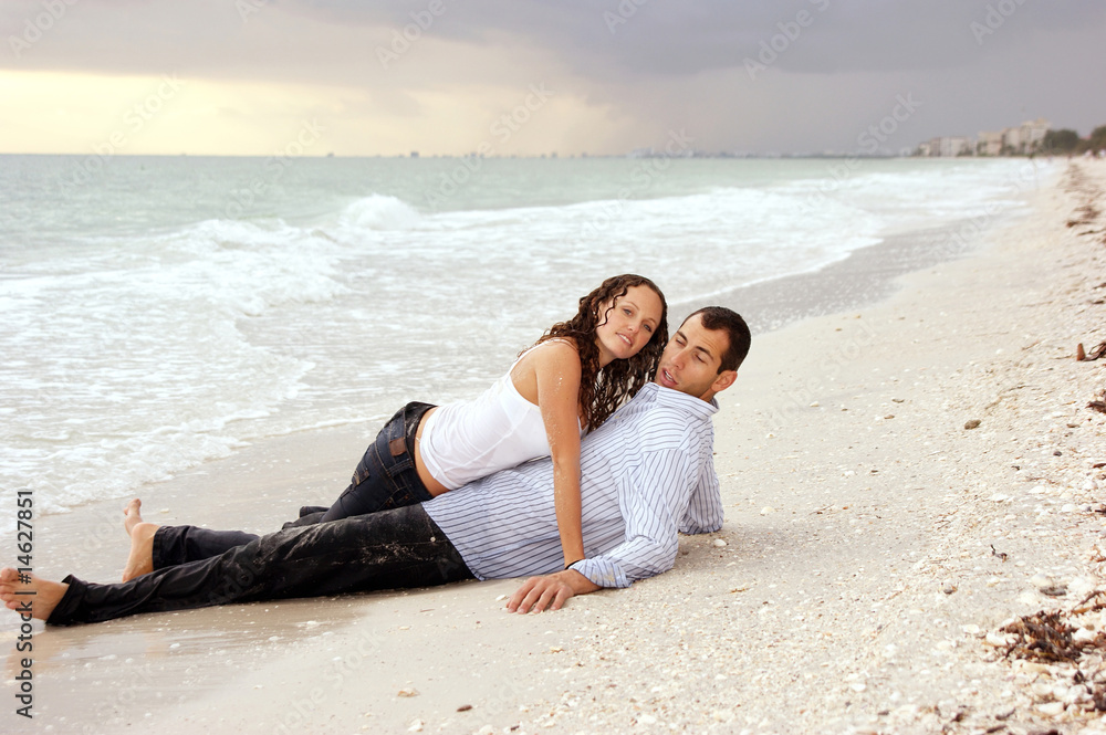 woman laying on top of man at beach looking at viewer
