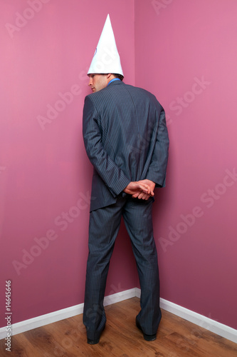 Businessman standing in the corner in a dunce hat