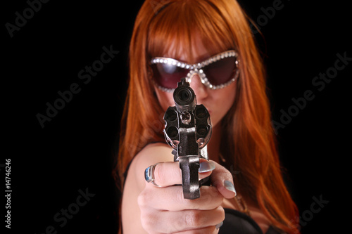 Young redhead woman with gun on black background