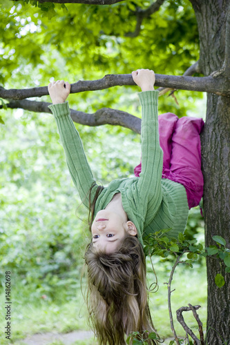 little cute girl hanging from branch of tree. Summer time