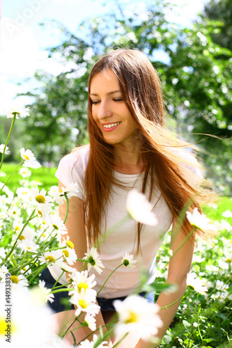 The young beautiful woman sits on a green field on which camomil photo