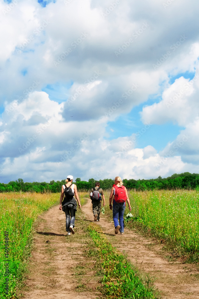 Group of three tourists with backpacks going in hikers walk on r Group of three tourists with backpacks going in hikers walk on r