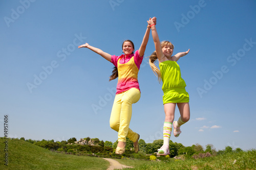 Two girls jumping on green meadow