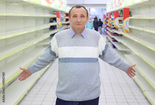 Foto elderly man stands between empty shelves in  shop with dissolved