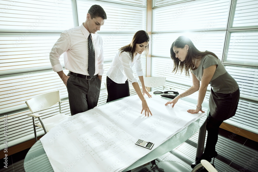 Professionals looking at architectural plans on desk Professionals looking at architectural plans on desk