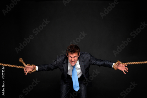 Businessman being pulled by rope on both sides.