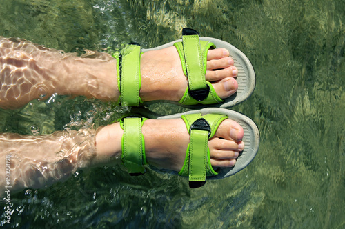 Two tanned feet with green sandal at the water