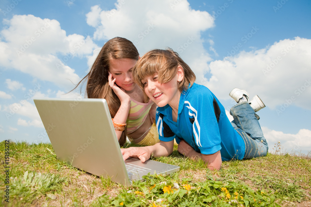 Two Smiling teenagers with laptop resting on meadow Two Smiling teenagers with laptop resting on meadow