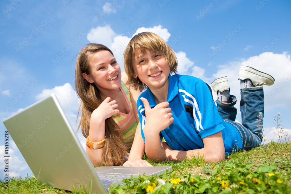 Two Smiling teenagers with laptop resting on meadow. Two Smiling teenagers with laptop resting on meadow.