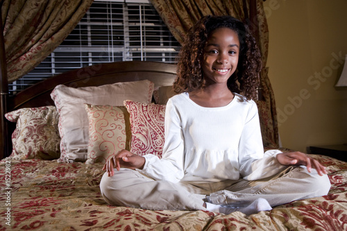 Cute 10 year old African American girl sitting on bed