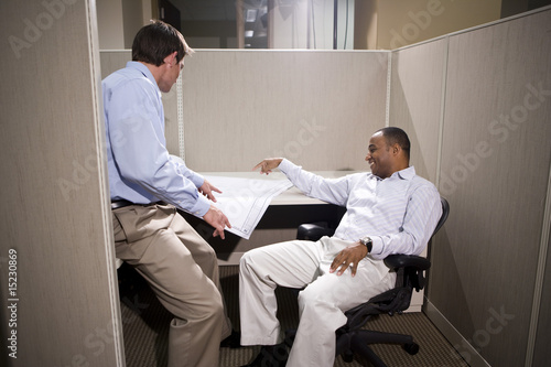 Two male office colleauges in cubicle discussing blueprints photo
