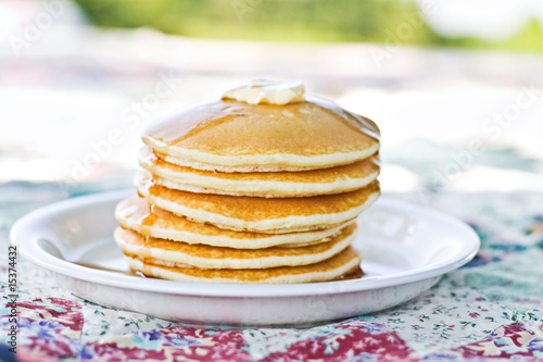 Stack of pancakes with syrup served outdoors.