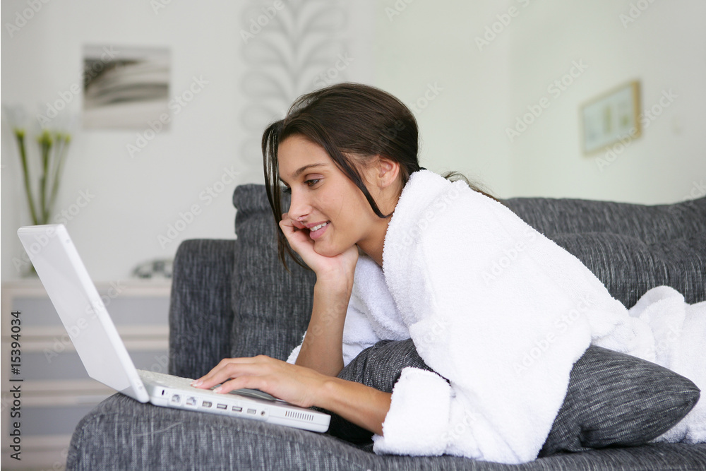 Femme en peignoir étendue sur un canapé devant un ordinateur Femme en peignoir étendue sur un canapé devant un ordinateur
