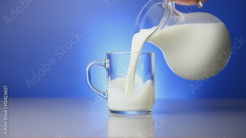 Milk being poured in glass on blue background