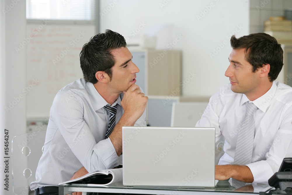 Hommes d'affaires au bureau discutant devant un ordinateur Hommes d'affaires au bureau discutant devant un ordinateur