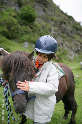 Enfant avec une bombe d'équitation caressant un poney