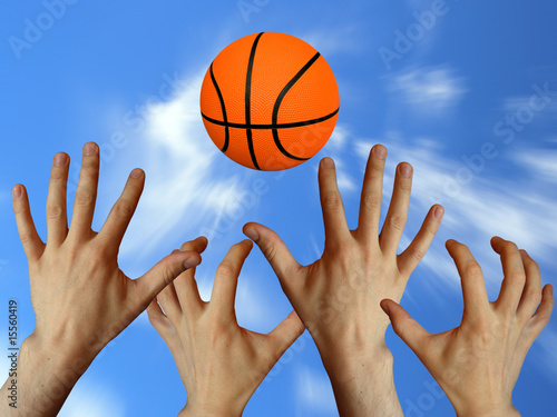 raised hands trying to catch orange basketball ball