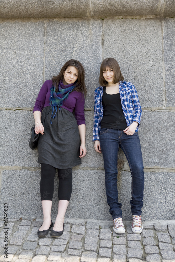 two urban teen girls standing at wall.