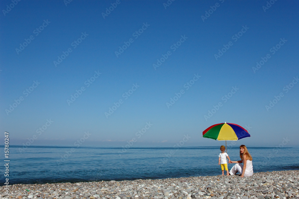 Woman with child under umbrella on seaside