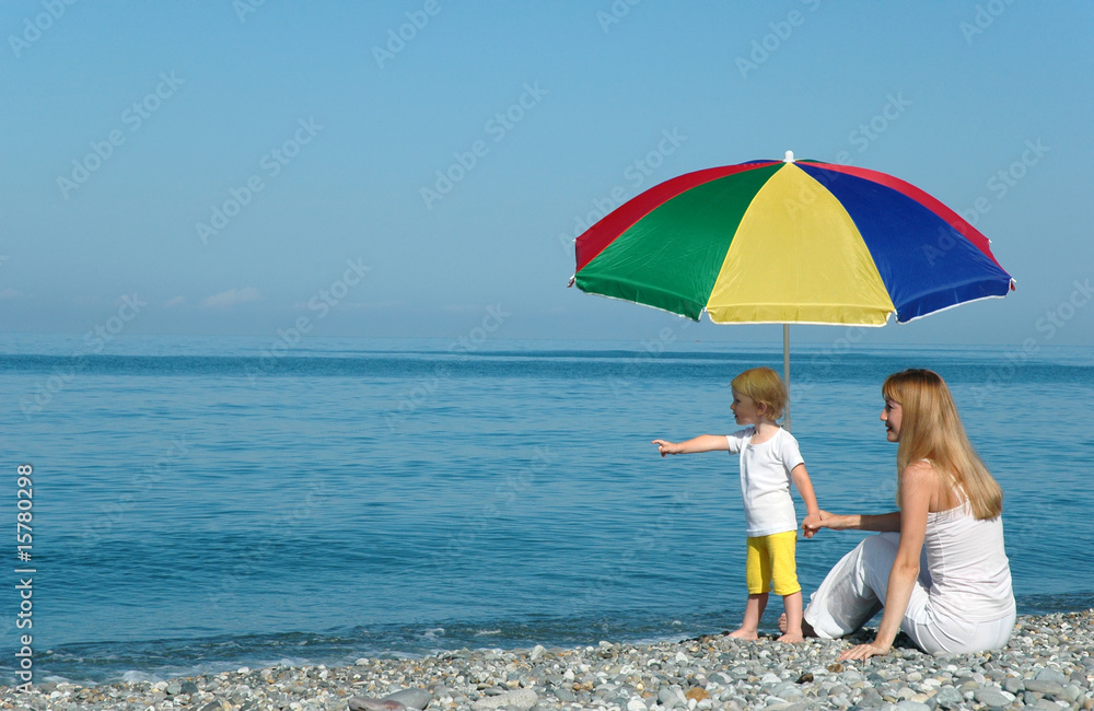 Woman with child under umbrella on the beach