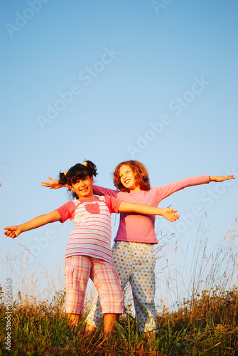 Two happy female children standing outdoor with hands up