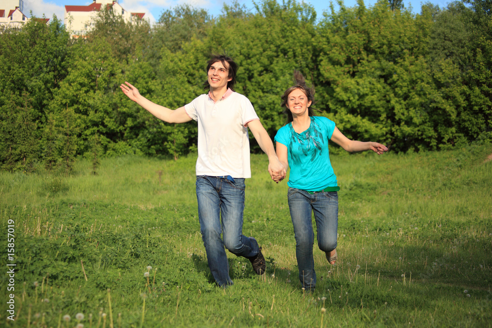 smiling young pair runs, keeping for hands, on grass in park smiling young pair runs, keeping for hands, on grass in park