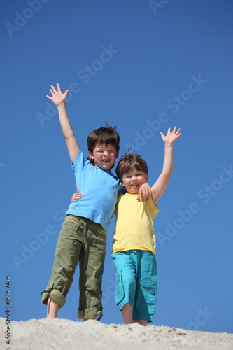 Two boys stand on sand and lifted hands in greeting