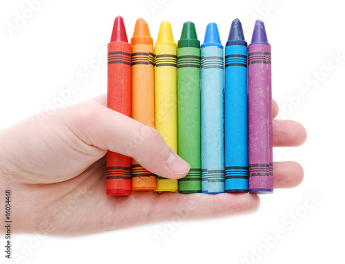 A hand holding a rainbow of colored crayons