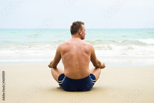 A forties man meditating and relaxing on a sandy beach.