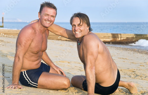 Two happy gay men sitting on the beach.