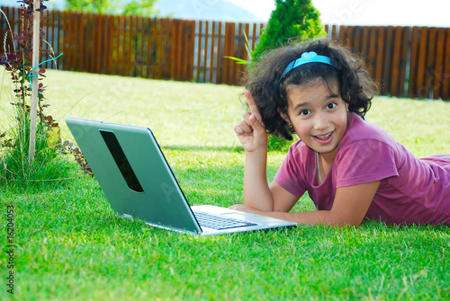 A little cute girl laying down in grass with laptop