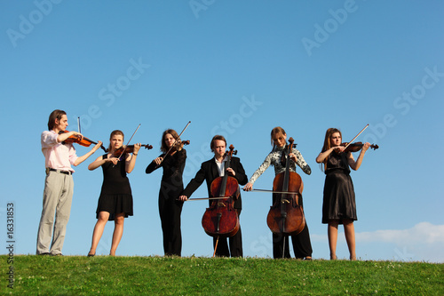 Six musicians play violins against sky