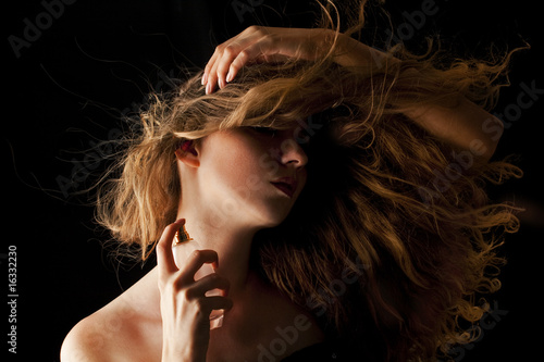 woman with flipping hair applying perfume on her body
