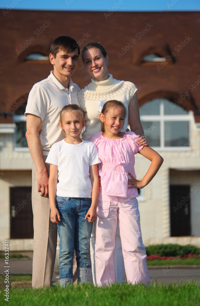 family from four stands on grass against house family from four stands on grass against house