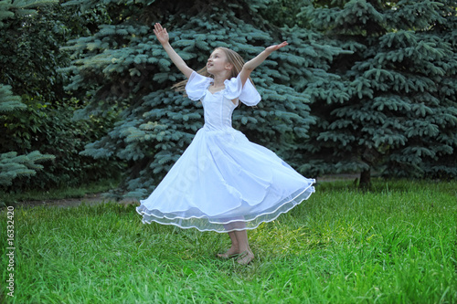 Fotografi girl in white dress dances on lawn with lifted hands