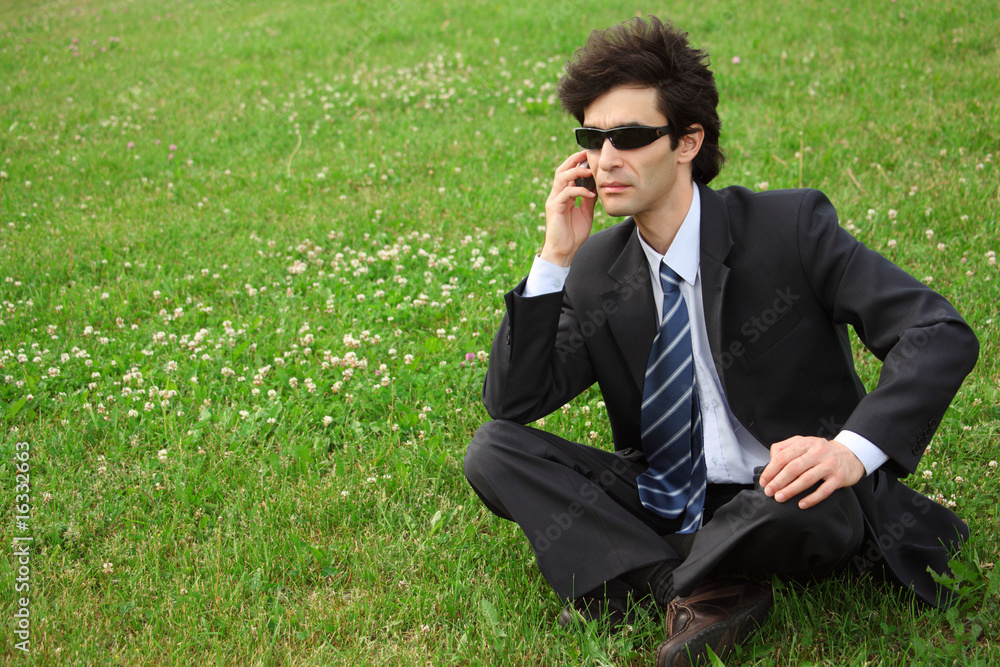 businessman speaks by phone sitting on grass businessman speaks by phone sitting on grass