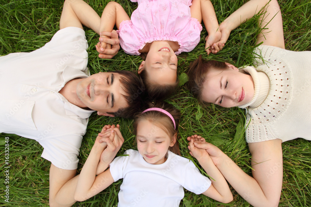 Parents with children lying on grass, view from top, head to hea Parents with children lying on grass, view from top, head to hea
