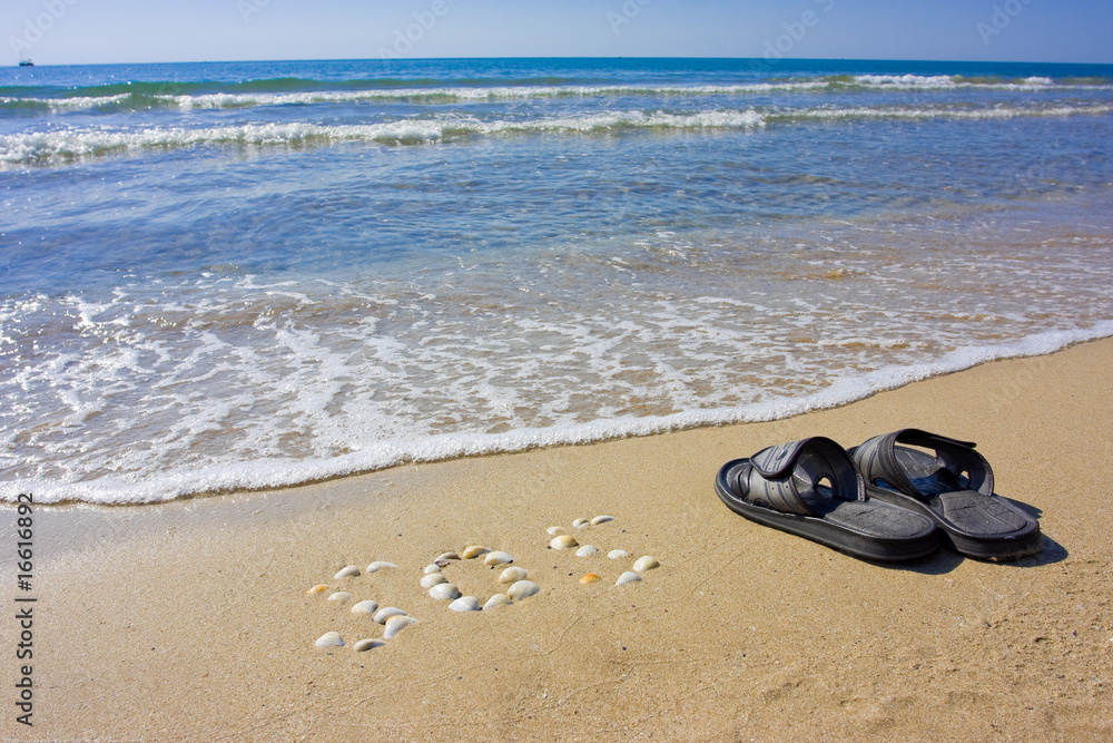 Obraz premium Inscription SOS in the sand with slippers and boat on skyline