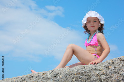 little girl sits on rock against sky photo