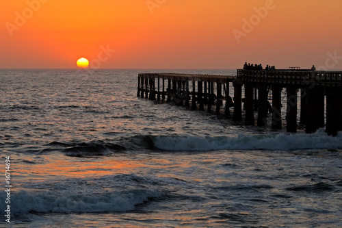 Silhouetted coastal pier with a glowing sunset