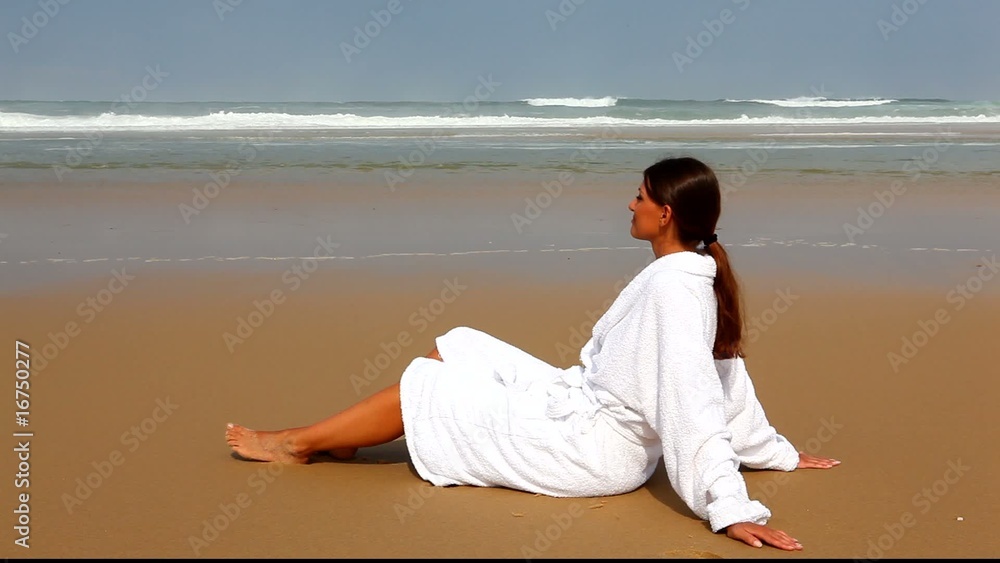 Jeune femme assise en peignoir sur la plage Jeune femme assise en peignoir sur la plage