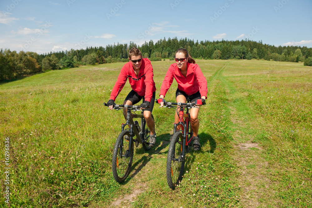 Sportive couple riding mountain bike in meadow Sportive couple riding mountain bike in meadow