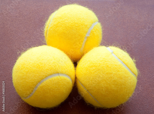 three tennis balls together in yellow on brown background.three photo