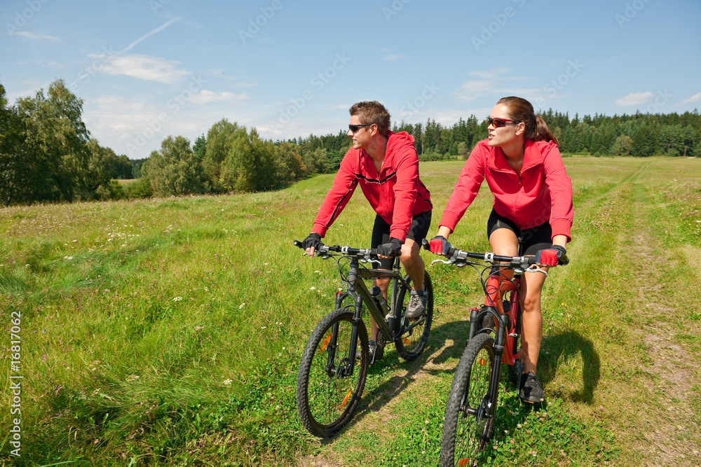 Sportive couple riding mountain bike in meadow