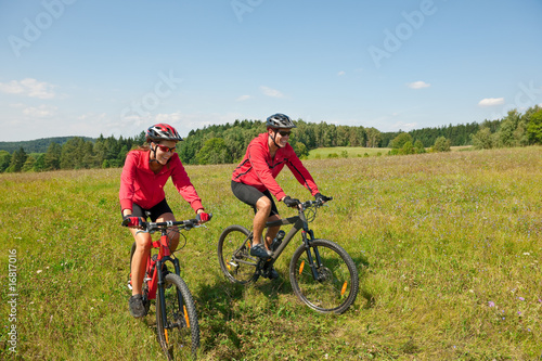 Fototapeta Naklejka Na Ścianę i Meble -  Sportive couple riding mountain bike in meadow