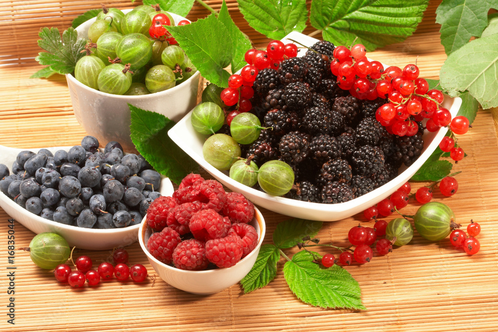 Berries in plates, on a table, among green leaves Berries in plates, on a table, among green leaves