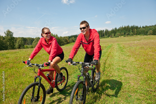 Sportive couple riding mountain bike in meadow