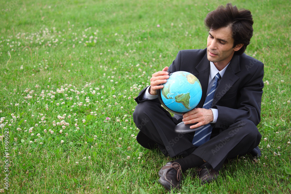 businessman sitting on the meadow and holding the globe businessman sitting on the meadow and holding the globe