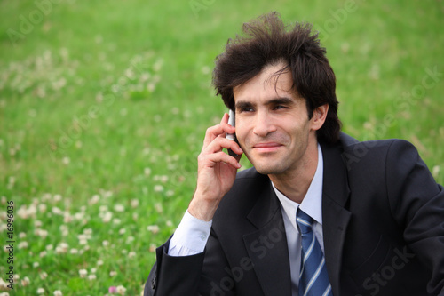 Businessman sits on the meadow and speaks over mobile