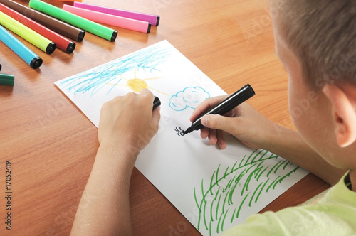 child draws green grass and sun on paper